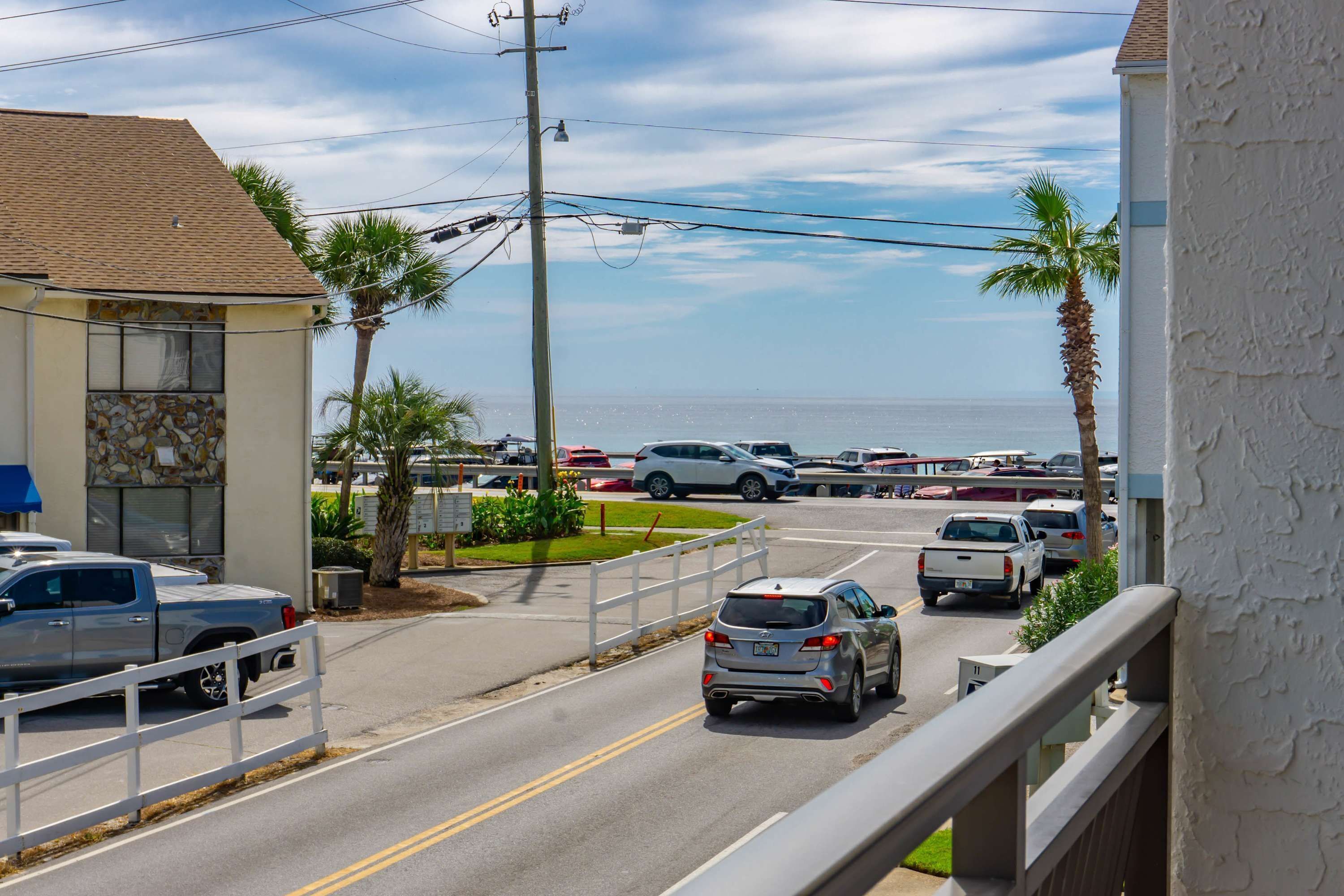A coastal road with parked vehicles, a clear sky, and a view of the ocean.