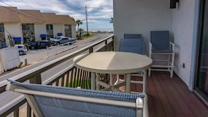 A balcony with a round table and two chairs, overlooking a street with parked cars and a building with blue awnings. - Beachfront Villa With Sea Views Bikes Included Gulf Across St Kayak Access (Miramar Beach)