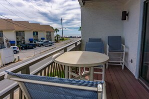 A balcony with a round table and two chairs, overlooking a street with parked cars and a building with blue awnings. - Beachfront Villa With Sea Views Bikes Included Gulf Across St Kayak Access (Miramar Beach)