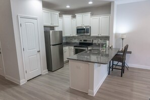 A kitchen with white cabinets, stainless steel appliances, a granite countertop, and a wooden floor. - Waterfall Community 109 Harmony Falls Lane Pets OK (Panama City Beach)