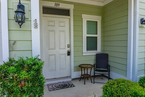 A green house with a white door, a small porch with a chair, and a window. - Waterfall Community 109 Harmony Falls Lane Pets OK (Panama City Beach)