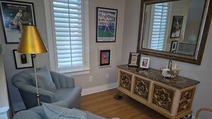 Een zithoek met een blauwe fauteuil, een vloerlamp, een decor kast en een grote spiegel.