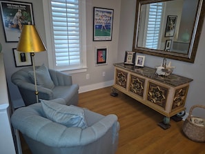 A living room with a blue armchair, a floor lamp, a decorative cabinet, and a large mirror. - Gated Beach Villa w 2 Pools 3 Bikes Included Tennis Pickleball Courts Included (Miramar Beach)