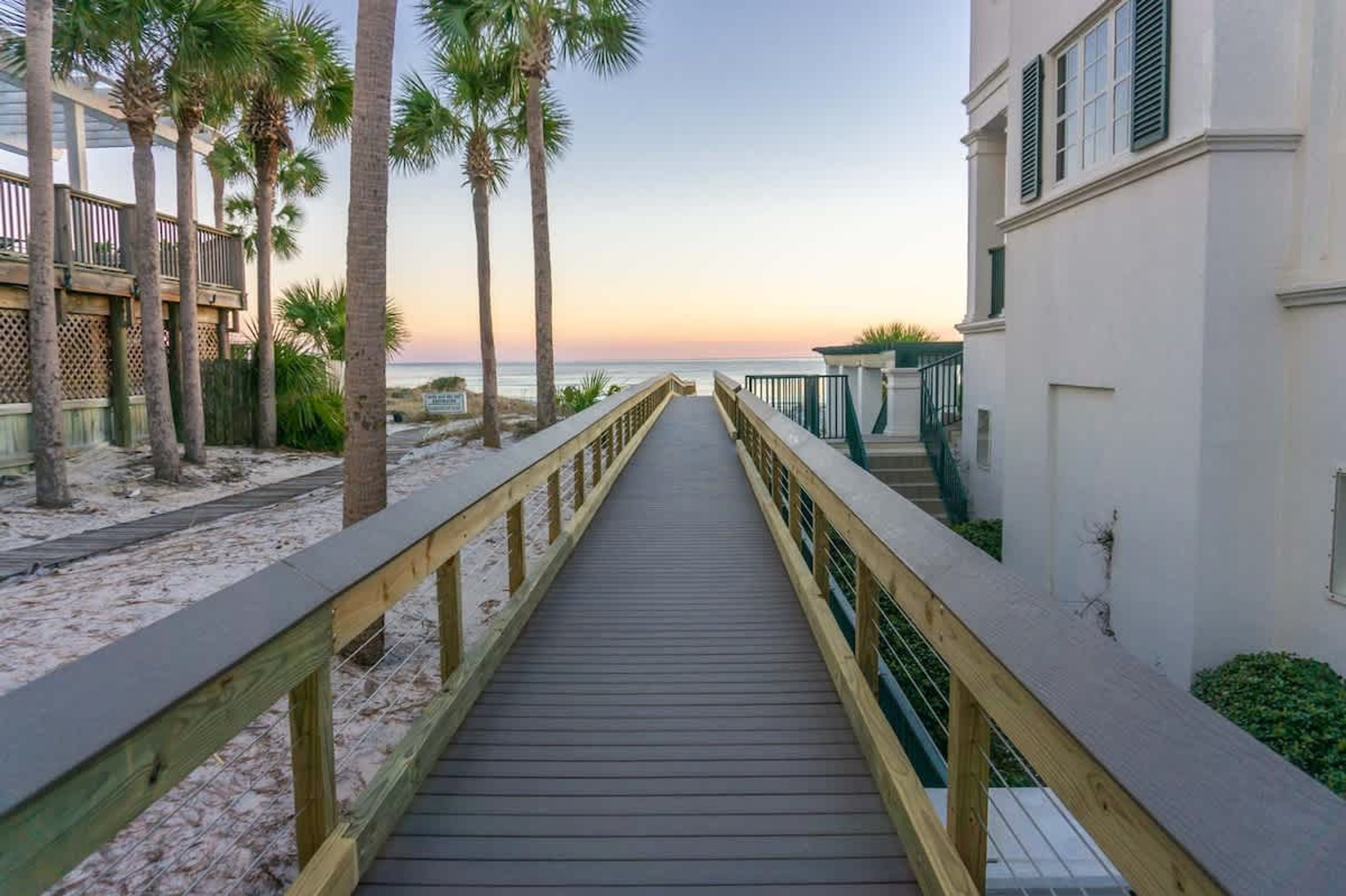 Une promenade en bois menant à une plage bordée de palmiers et à un bâtiment doté d’un balcon.