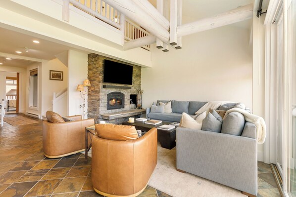 A spacious living room with a stone fireplace, leather sofas, and a large window.