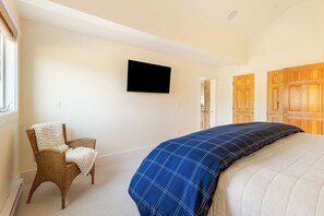 Ein Schlafzimmer mit einem Bett, einem Sessel, einem Fernseher und Holztüren.