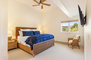 Une chambre à coucher avec un lit en bois, des lampes de chevet, une fenêtre donnant sur un beau paysage et un ventilateur de plafond.
