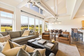 A spacious living room with a large sofa, a coffee table with books, and a dining area with chairs and a table.