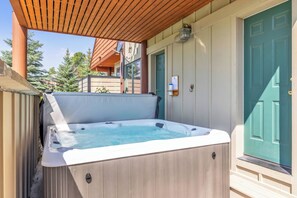 A hot tub with a wooden exterior, a door with a green handle, and a wooden pergola overhead.