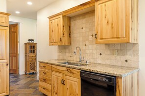 A kitchen with wooden cabinets, granite countertops, a dishwasher, and a tiled backsplash.