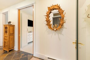 Un couloir avec une armoire en bois, un miroir doté d’un cadre en forme de feuille et une porte donnant sur une autre pièce.