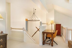 A room with a staircase, a table with a chair, a lamp, and a wooden cabinet.
