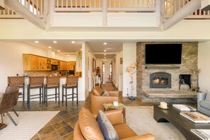 A spacious living area with a fireplace, a kitchen with wooden cabinets, and a high ceiling with exposed beams.