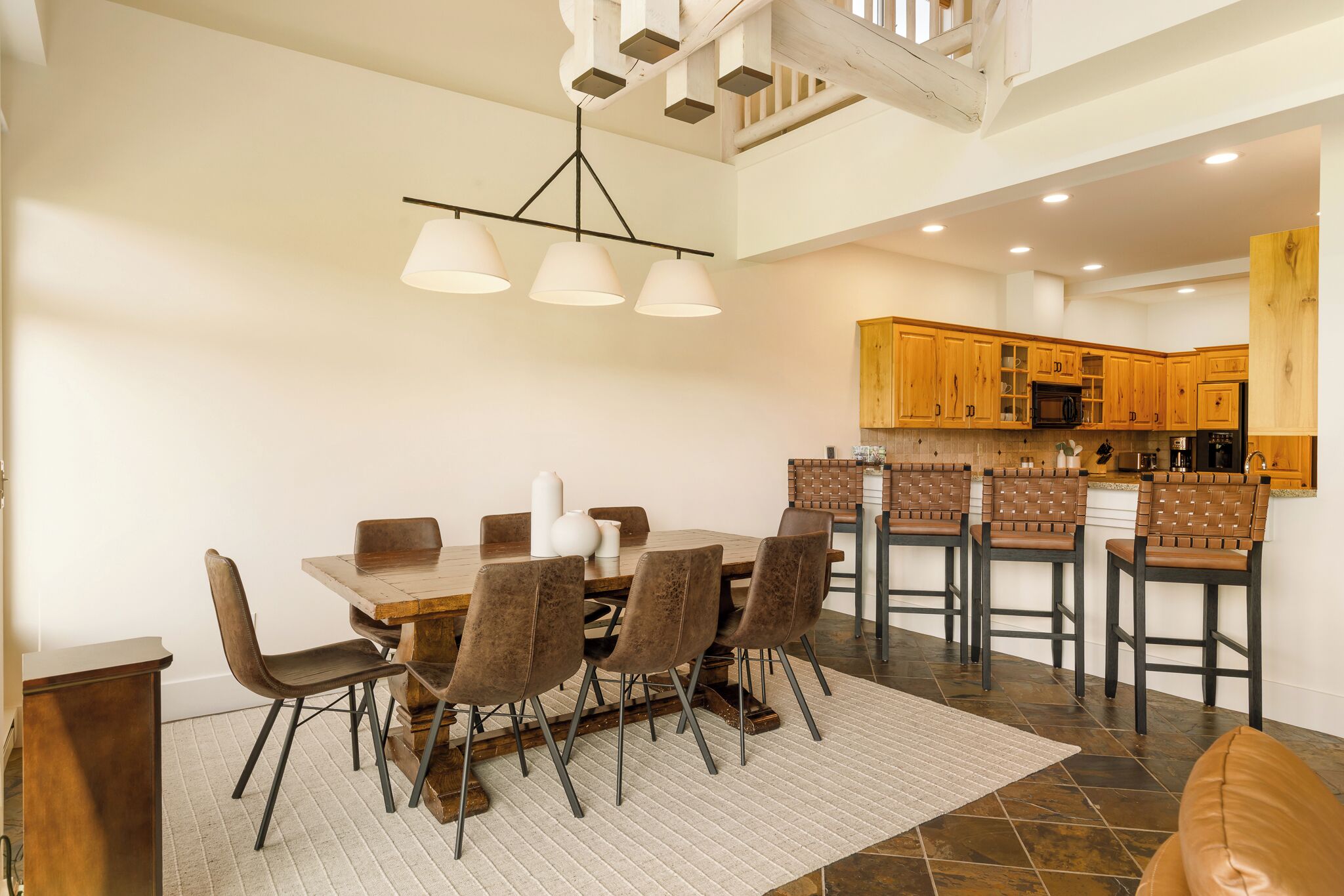 A dining area with a wooden table and chairs, a kitchen with wooden cabinets, and a staircase leading to an upper level.