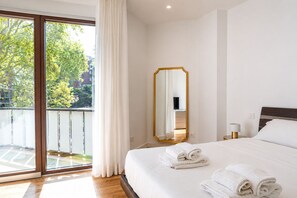 Ein Hotelzimmer mit einem großen Bett, einem Spiegel, einem Nachttisch und Blick ins Freie durch eine Schiebetür.