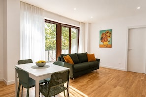 A dining area with a table, chairs, and a bowl of fruit. There is a sofa with cushions and a painting on the wall. - Elegantis Luce di Trastevere Apartment with Terrace (Roma)