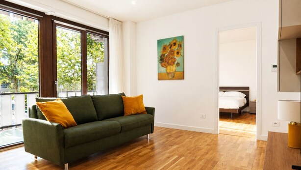Een kamer met een groene bank, een schilderij aan de muur en een bed op de achtergrond.