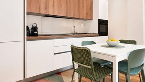 Een moderne keuken met witte kasten, een houten bovenkast, een zwarte oven en een eettafel met stoelen.