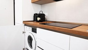 Een compacte keuken met een ingebouwde wasmachine, een houten aanrechtblad en een zwarte tas op het aanrecht.