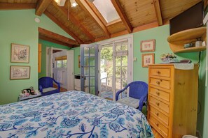 Een slaapkamer met een bed, een dressoir, een stoel en een deur die leidt naar een buitenruimte.