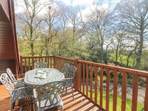 A wooden deck with a round table and chairs, overlooking a green landscape with trees. - Honeycombe Lodge (Gunnislake)