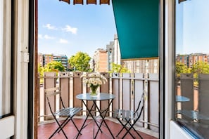 A balcony with a table and chairs, a vase of flowers, and a view of buildings and trees. - Elegantis Trastevere Suite with Terrace - Comfort in Most Charming District (Roma)