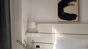Ein Hotelzimmer mit einem Bett, einem Nachttisch mit Pflanze, einem Wandbild und einem Thermostat.