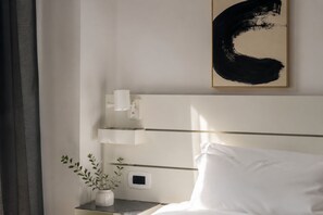 Ein Hotelzimmer mit einem Bett, einem Nachttisch mit Pflanze, einem Wandbild und einem Thermostat.