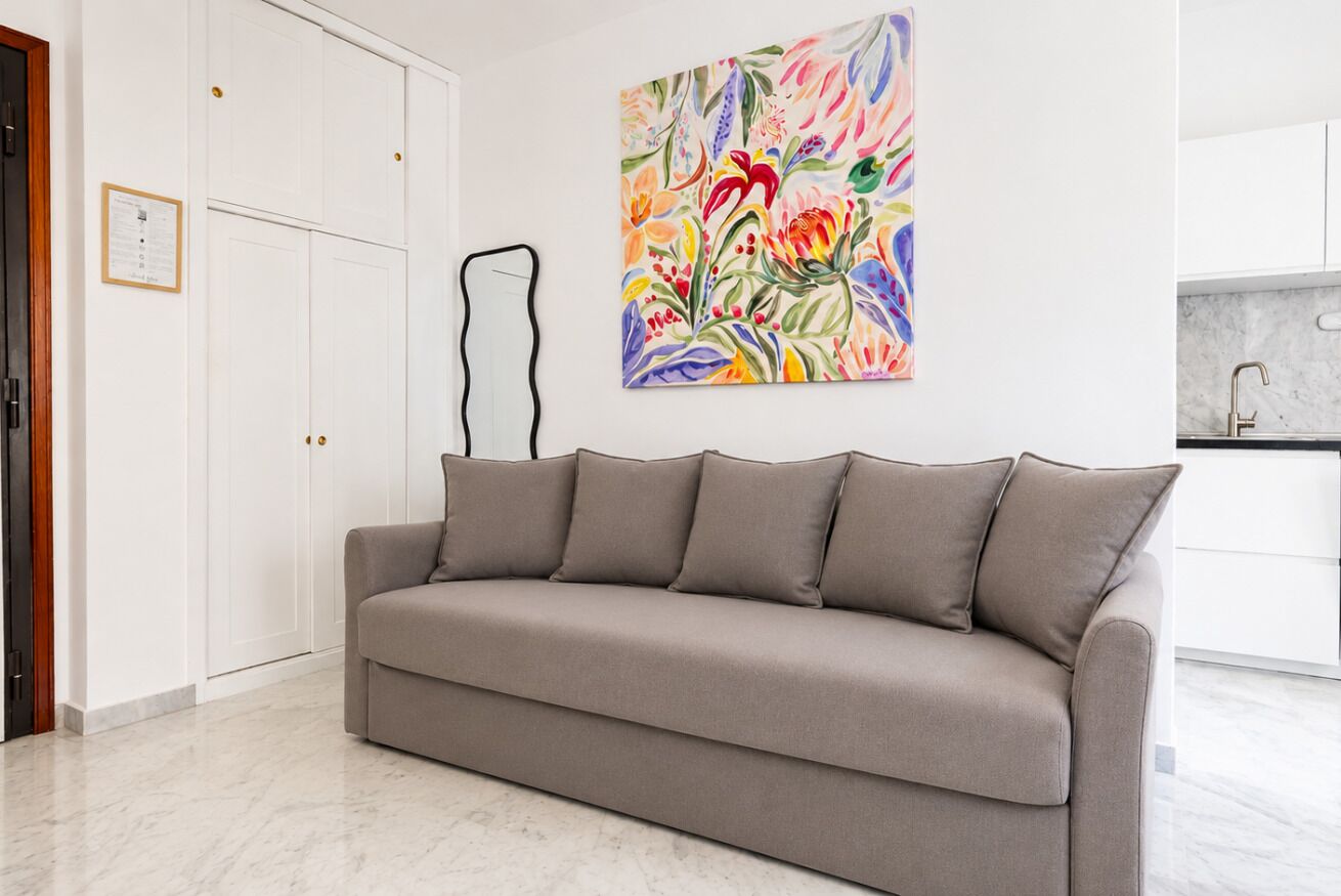 Un divano dai toni neutri in un soggiorno moderno, con un quadro astratto dai colori vivaci appeso alla parete.