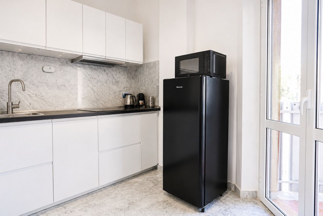 Una cucina moderna con mobili bianchi, un frigorifero nero e un forno a microonde.