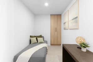 Ein kleines, modernes Schlafzimmer mit einem Bett, einem Holzschrank und einem Nachttisch mit Pflanze.