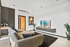 A modern living room with a sectional sofa, a flat-screen TV, a wooden door, and a minimalist decor. - Hooiberg 49 U Apt 1 Pearl House (Oranjestad)