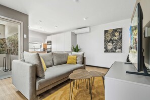 Ein modernes Wohnzimmer mit einem grauen Sofa, einem kleinen Holztisch und einem Fernseher auf einem Schrank.