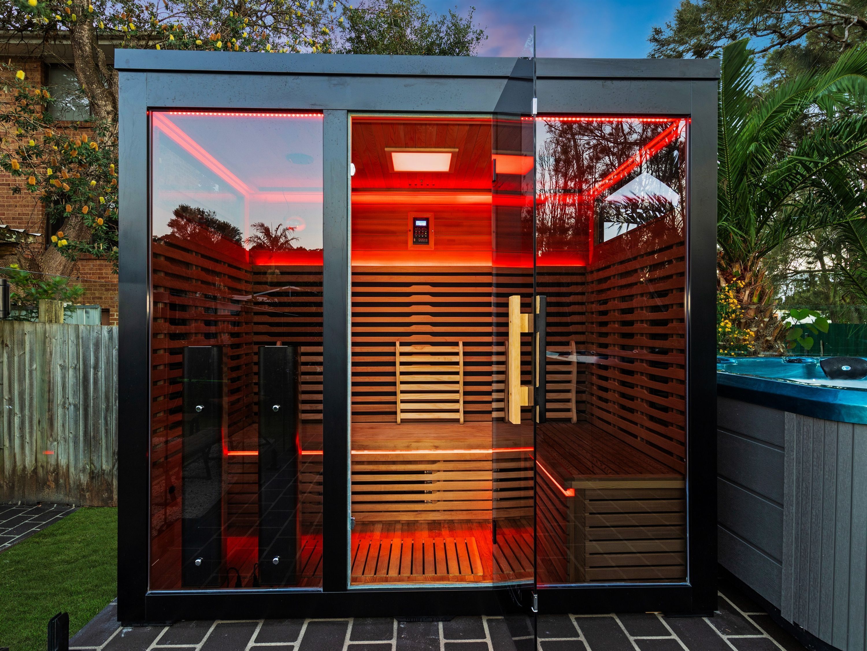 A modern sauna with glass walls, a wooden bench, and a control panel.