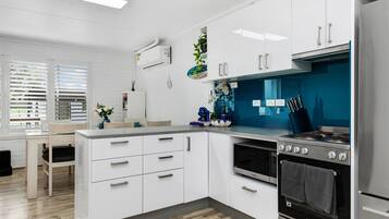 Cozinha moderna com armários brancos, fogão de aço inoxidável e painel de fundo azul.