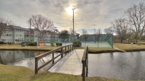 A wooden bridge over a calm water body, surrounded by grass and trees, with buildings in the background. - Charming 2BR for 6! Steps to Beach! MBR 346A (Myrtle Beach)