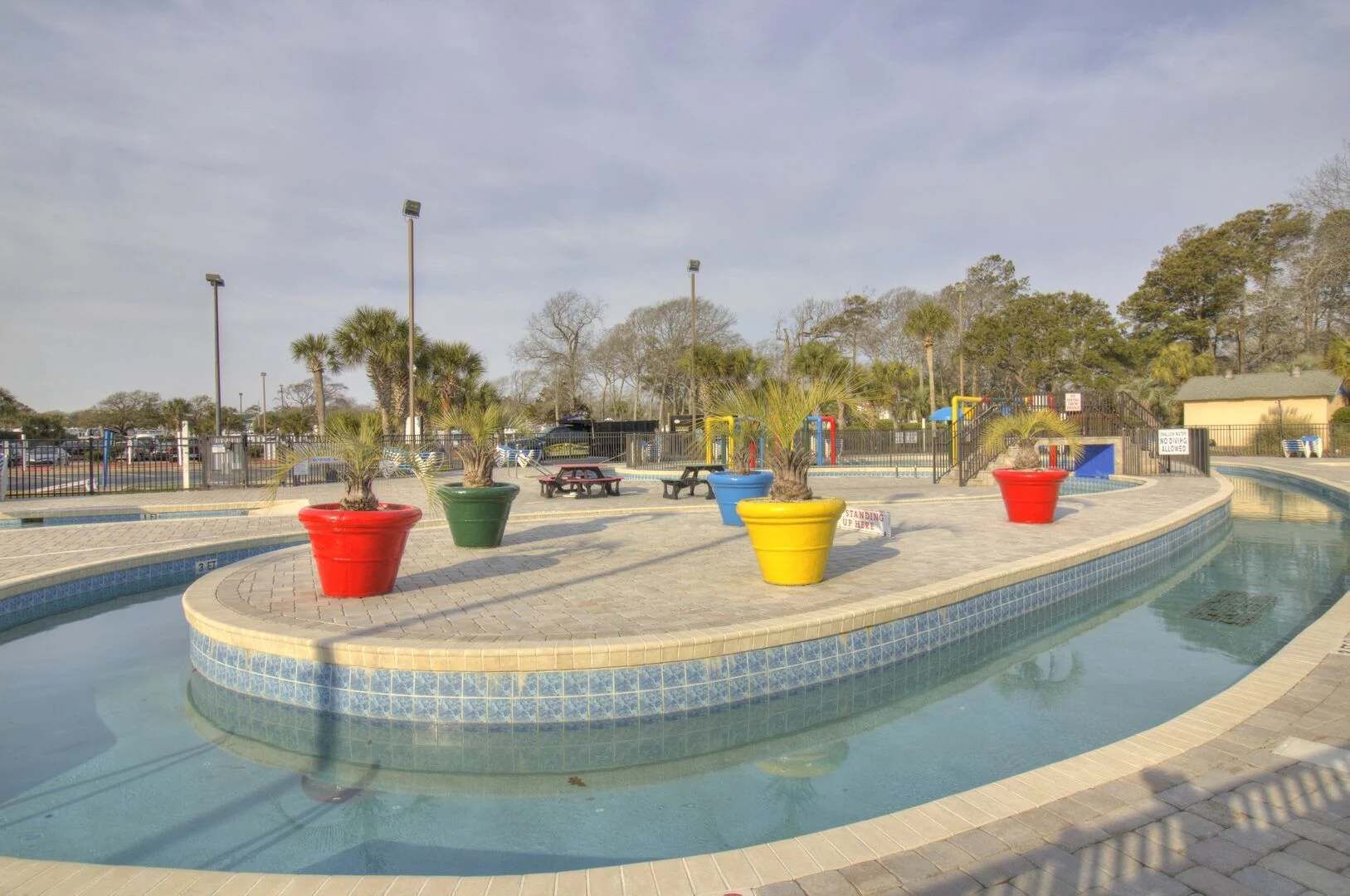 A swimming pool with a tiled edge, surrounded by potted plants and benches.