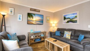 A living room with two grey sofas, a wooden coffee table, a TV mounted on the wall, and a wooden shelf with decorative items. - Charming 2BR for 6! Steps to Beach! MBR 346A (Myrtle Beach)