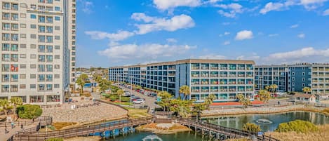 A modern building complex with multiple floors, a parking area, and a water feature with a bridge.