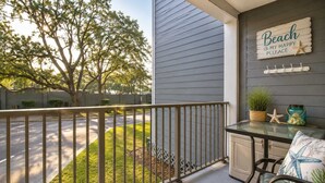 A balcony with a view of a tree, a sign reading 'Beach is my happy place,' and a small table with a starfish decoration. - Charming 2BR for 6! Steps to Beach! MBR 346A (Myrtle Beach)