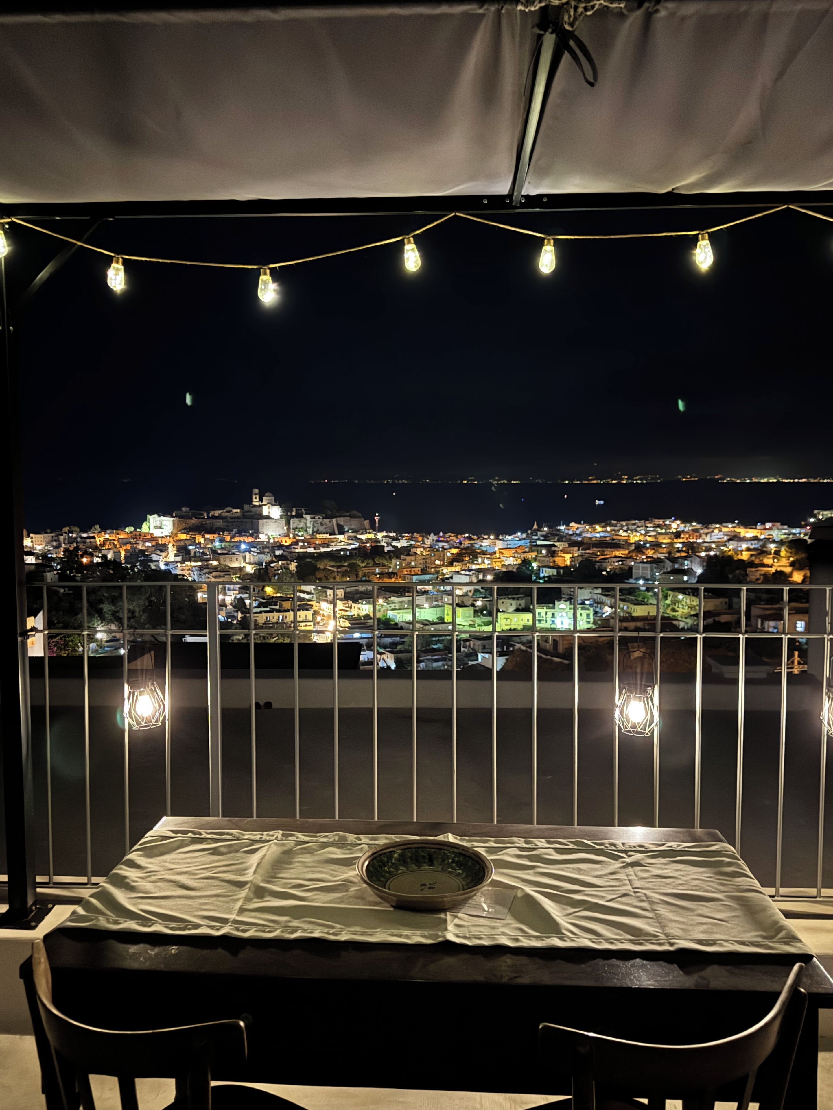 Ein Balkon mit Tisch und Stühlen, der auf eine nächtliche Skyline blickt.