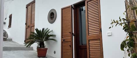 Un edificio con fachada blanca, contraventanas de madera, una planta en maceta y una pequeña ventana circular.
