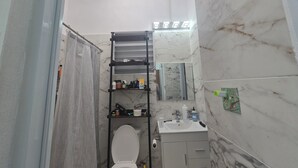 Un baño con inodoro, repisa con artículos de aseo, espejo y pared de mármol.