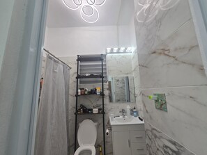 A bathroom with a toilet, a shelf with toiletries, a mirror, and a marble wall. - Delightful 2-bedroom house with AC and parking in Aguadilla (Aguadilla)