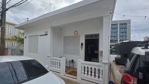 Un edificio blanco con un letrero con el número '32', un balcón con barandilla y un vehículo estacionado frente a él.