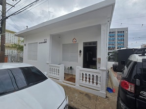 A white building with a number '32' sign, a balcony with railings, and a vehicle parked in front. - Delightful 2-bedroom house with AC and parking in Aguadilla (Aguadilla)