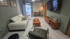 Una sala de estar con un sofá, una mesa de centro, un televisor y un escritorio con una lámpara.
