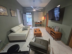 A living room with a sofa, a coffee table, a TV, and a desk with a lamp. - Delightful 2-bedroom house with AC and parking in Aguadilla (Aguadilla)