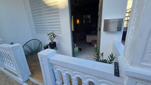 Fachada blanca con el número '32' en una pared, una planta en maceta y una silla verde.