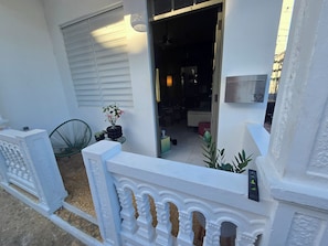 A white exterior with a number '32' on a wall, a potted plant, and a green chair. - Delightful 2-bedroom house with AC and parking in Aguadilla (Aguadilla)